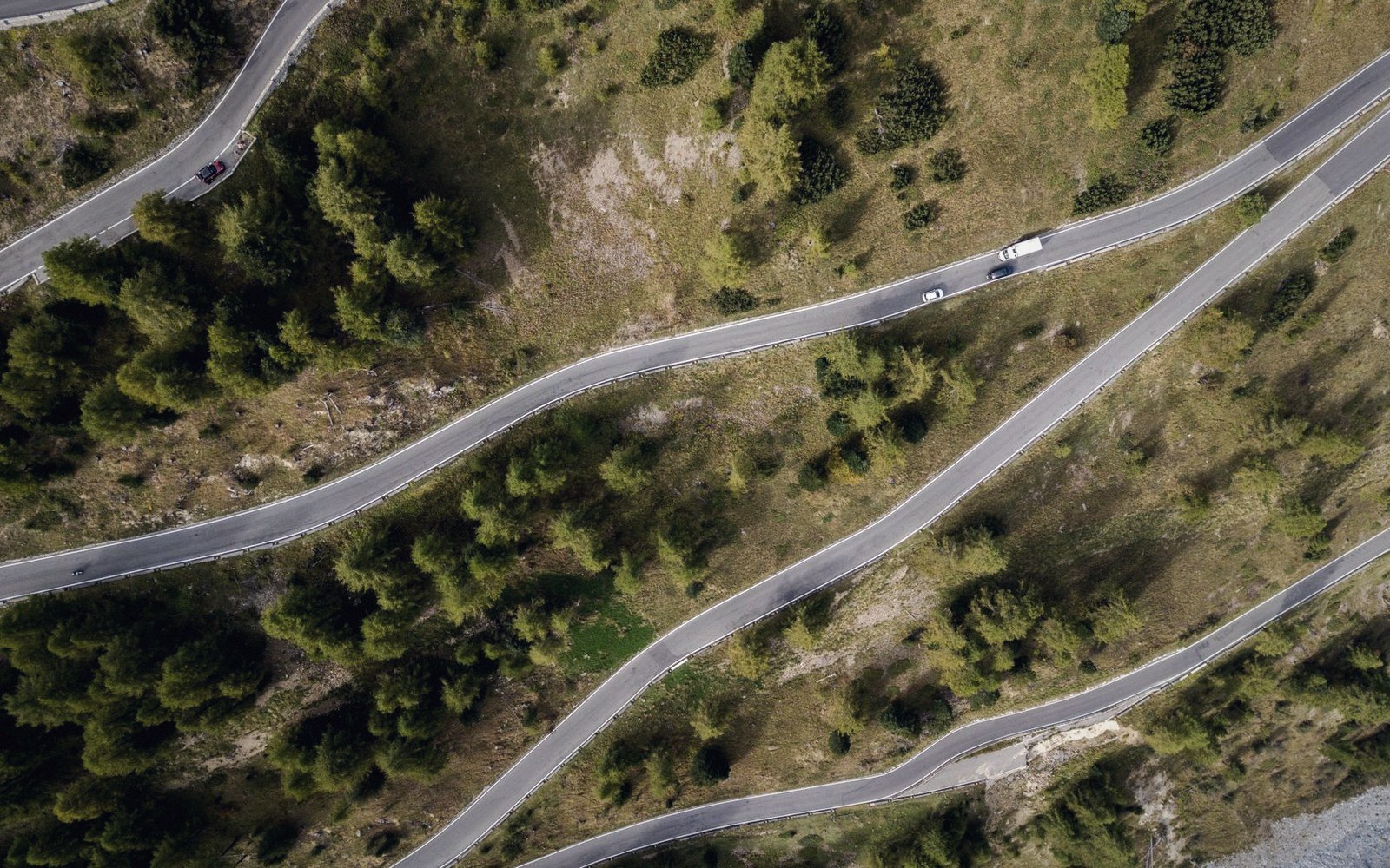 A two-lane asphalt road switchbacking up a forested mountain slope, no vehicles, overcast light