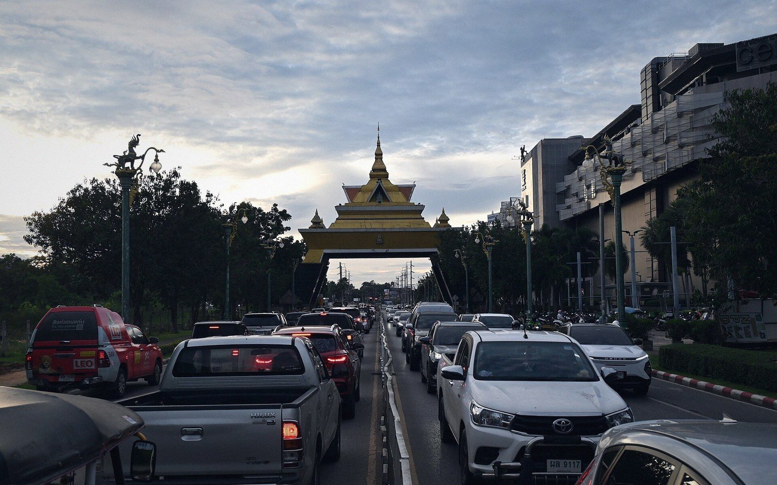 Traffic queues on a city road leading to an ornate golden archway gate