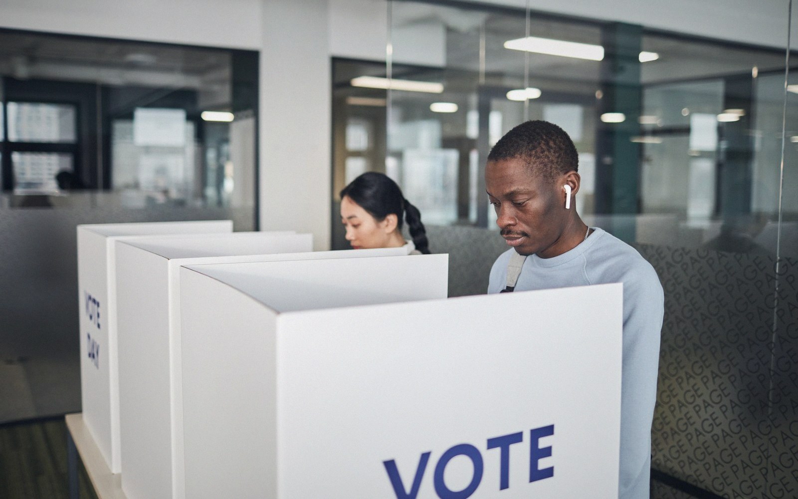 Two people fill out ballots at separate voting booths marked "vote"