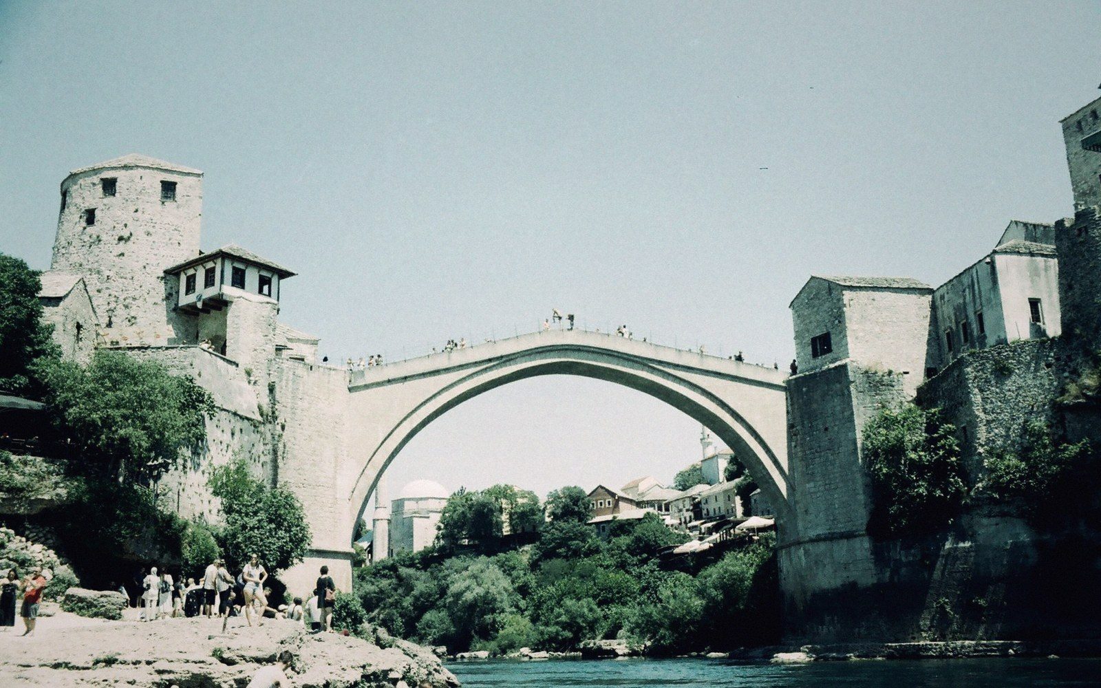 Stone arched bridge spans a river gorge between old stone towers and houses