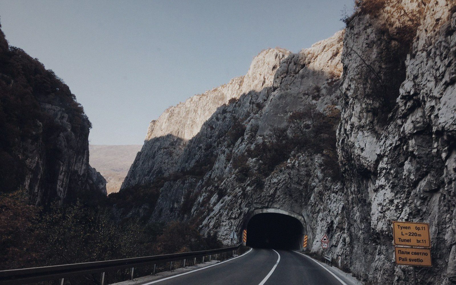 A mountain road curves toward a tunnel entrance cut through steep rocky cliffs