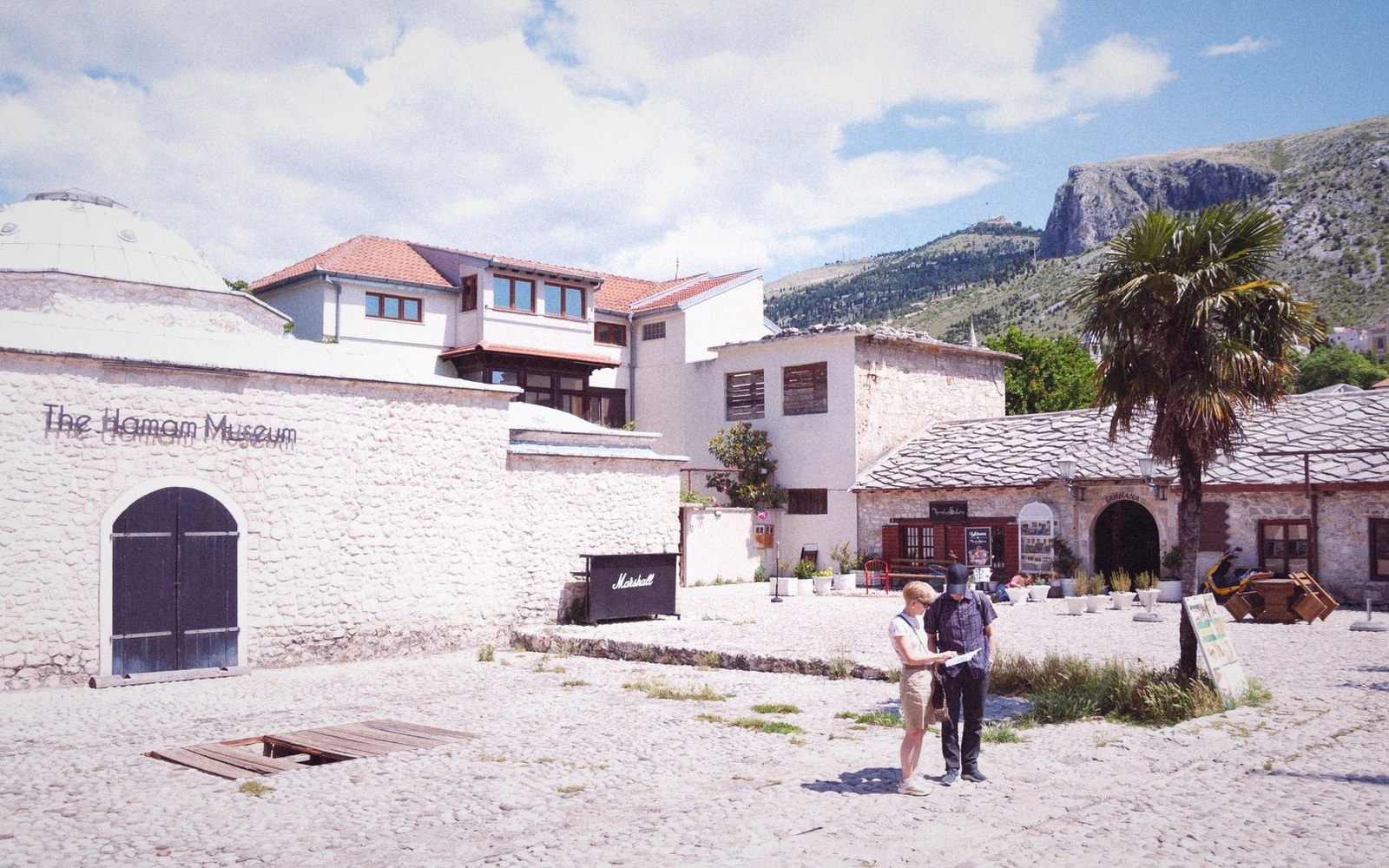 Visitors consult a map outside the Hamam Museum with mountains in the background