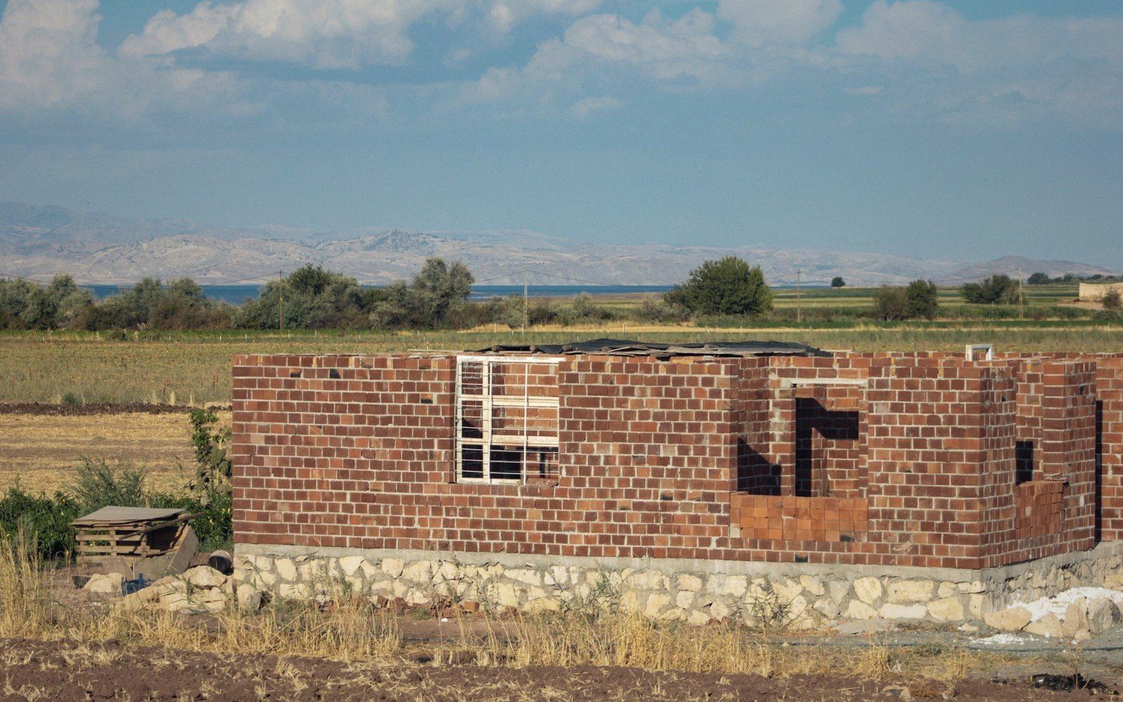 Unfinished brick house stands roofless amid farmland with distant lake and mountains