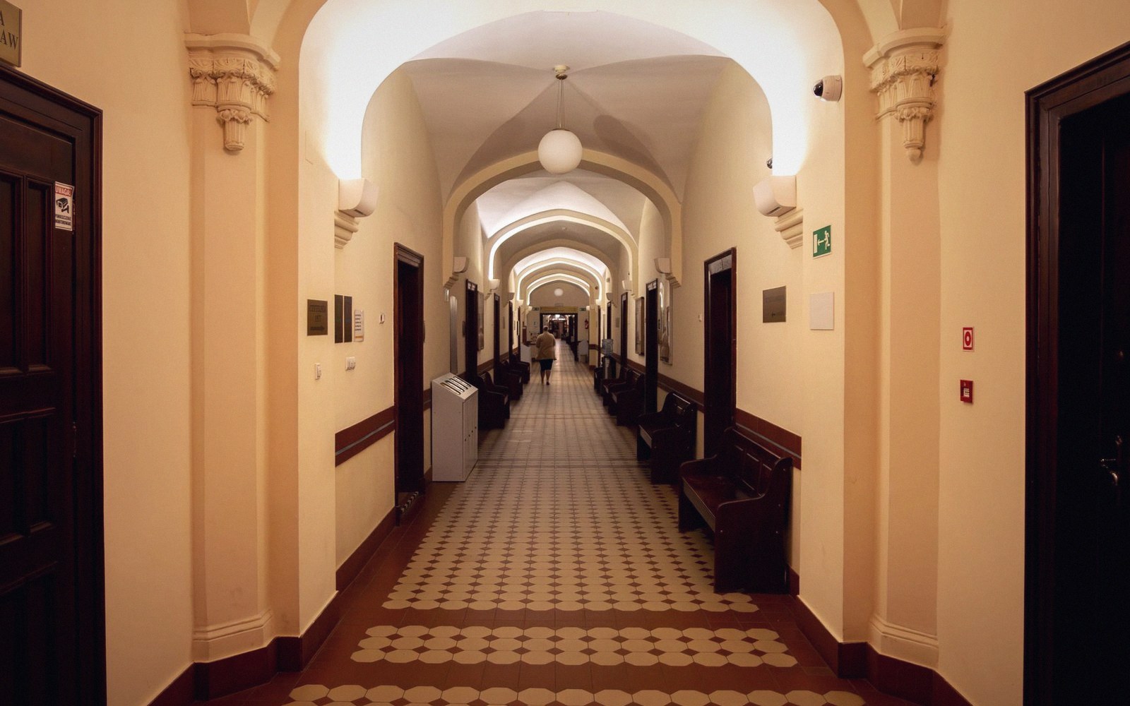 A vaulted corridor with patterned tile flooring and wooden benches lining the walls