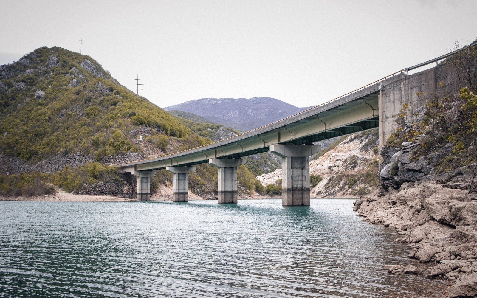 A concrete highway bridge on tall pillars spans a lake between rocky hills