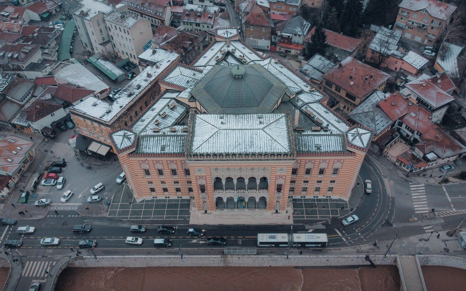 Aerial view of a domed riverside building with striped facade amid a snow-dusted city