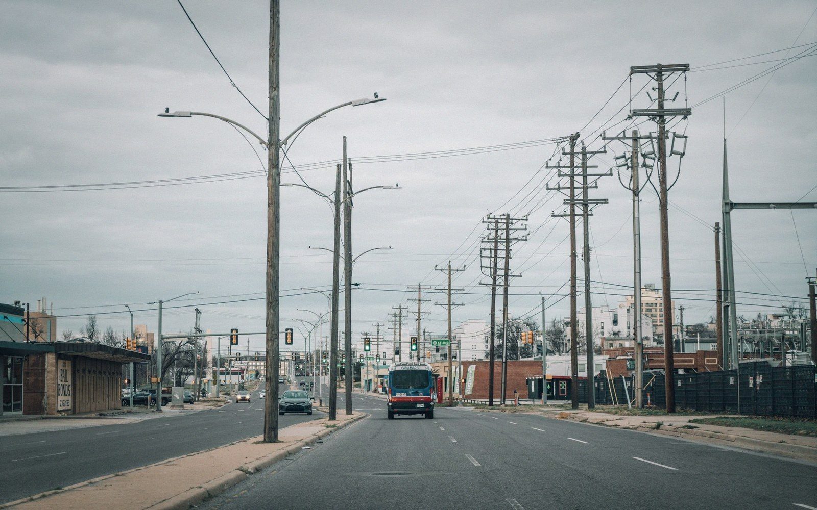 A close-up of power lines and communication cables strung between concrete poles on a village road, soft evening light