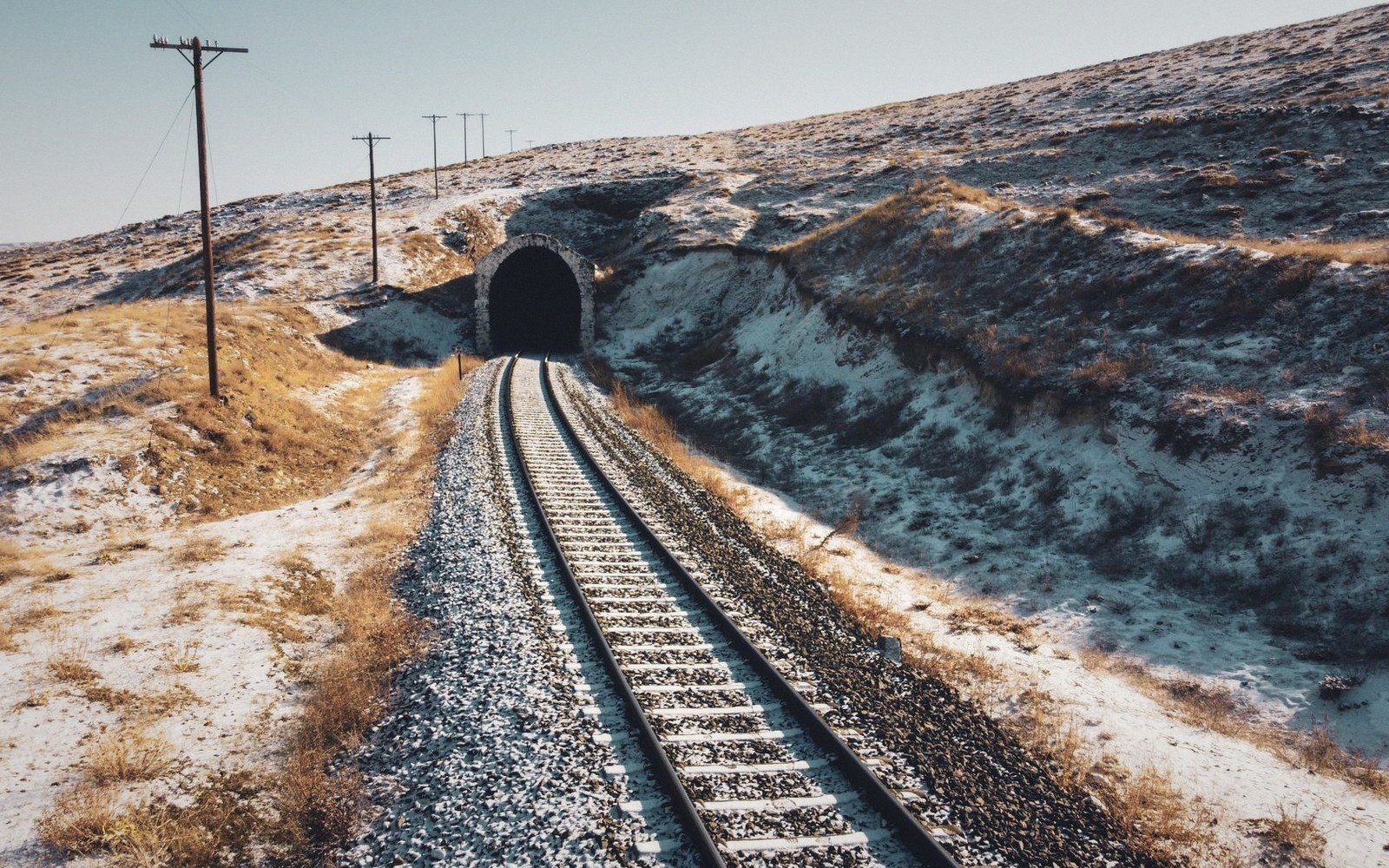 A single rail line cutting through white limestone karst, no train present, receding into a tunnel mouth in the distance